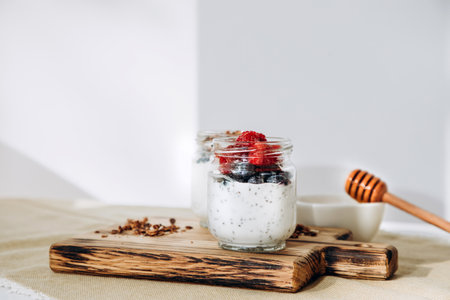 Yoghurts in glass jars with blueberries, raspberries and chia seeds and granola on a wooden board on...