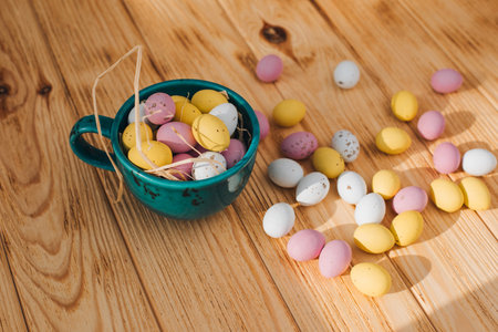 Multi-colored chocolate decorative eggs in blue mug with dry corn on a wooden background. Happy...