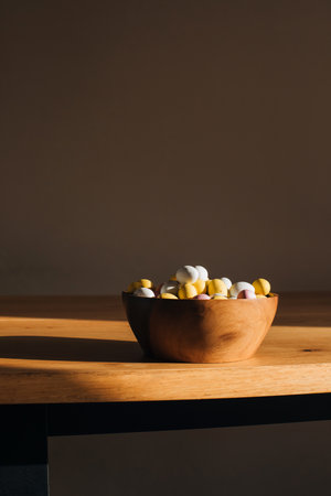 Multi-colored chocolate decorative eggs in wooden plate on a wooden table against brown wall with...