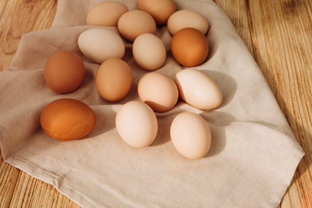 Chicken eggs of different brown and beige shades on a wooden background on grey kitchen towel....