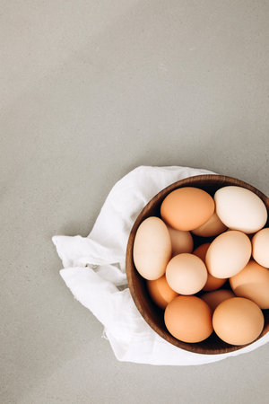 Chicken eggs of different brown and beige shades in a large wooden bowl on a grey background with...