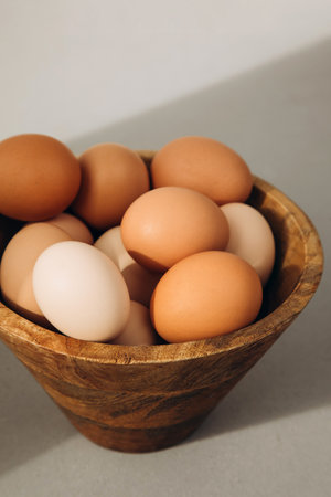 Chicken eggs of different brown and beige shades in a large wooden bowl on a grey background. Easter...
