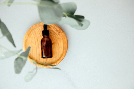 Amber bottle with facial cosmetics on a tray with a branch of eucalyptus on the gray concrete background, facial cleaner. Top viewの写真素材
