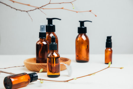 Set of natural cosmetics. Amber bottles with facial, bath liquid on a concrete background with young twigs of a tree. Front viewの写真素材