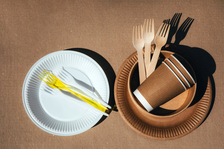 A set of paper utensils, wooden cutlery and plastic utensils on a brown background. Eco friendly, zero waste concept. Top viewの写真素材