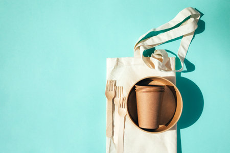 A paper utensils, plates and wooden cutlery on a textile bag on a blue background. Eco friendly pattern, zero waste concept. Top viewの写真素材