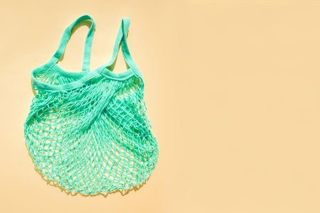 Reusable blue-green mesh bag on a beige background in sunny daylight. Mesh shopping bags. Sustainable use conceptの写真素材