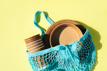 A set of paper utensils in mesh blue bag on a yellow background. Eco friendly, zero waste concept. Top viewの写真素材