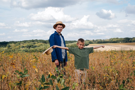 Agronomist, father and son together in agriculture field with soybeans. The man shows the boy ripe soy. Quality control of crops. Front viewの写真素材