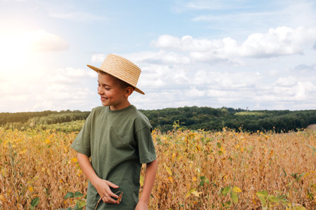 A school-age boy in the soybean field. Controlling the growth of agricultural crops. Yellow soy with beans. Front viewの写真素材