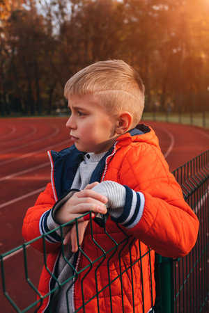 A boy in an orange jacket at the stadium. Autumn walk. Portrait of a child at sunset. Front viewの写真素材