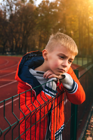 A boy in an orange jacket at the stadium. Autumn walk. Portrait of a child at sunset. Front viewの写真素材