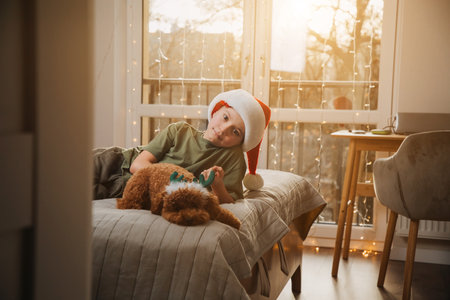 A boy in red Christmas hat with little puddle dog on the bag bad in bright sunlight. Children and pets. Portrait of a child. Front viewの写真素材