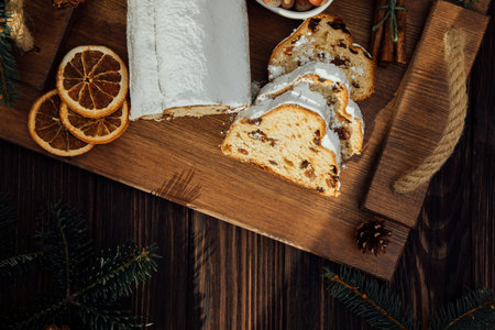 Christmas stollen on a wooden board with green branches of a Christmas tree on dark wooden...