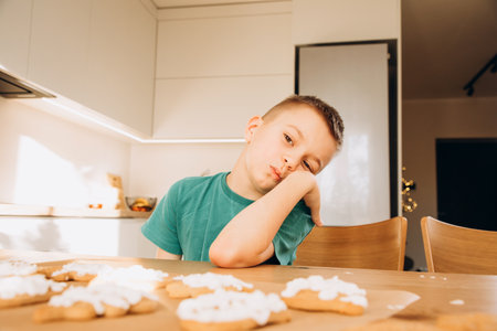 A school-age boy in the kitchen decorates Christmas cookies in sunny weather. Children in the kitchen, homemade pastries. Front viewの写真素材