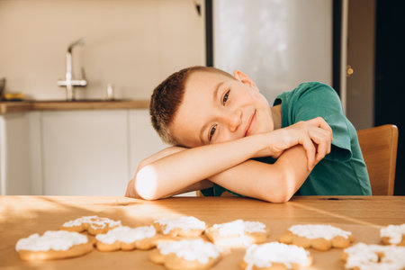 A school-age boy in the kitchen decorates Christmas cookies in sunny weather. Children in the kitchen, homemade pastries. Front viewの写真素材