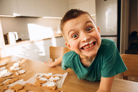 A school-age boy in the kitchen decorates Christmas cookies in sunny weather. Children in the kitchen, homemade pastries. Front viewの写真素材