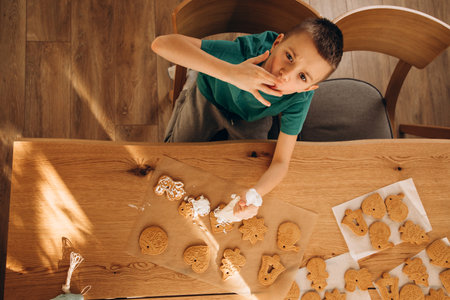 A school-age boy in the kitchen decorates Christmas cookies in sunny weather. Children in the kitchen, homemade pastries. Top viewの写真素材
