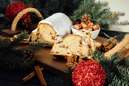 Christmas stollen on a wooden board with green branches of a Christmas tree on black wooden...