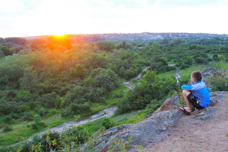 Boy looking to landscape in sunsetの写真素材
