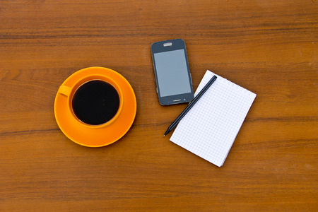 Coffee cup with smartphone, notepad and pen on the wooden desk