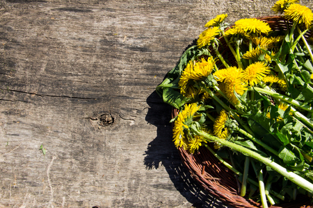 Yellow dandelion flowers in wicker basket on rustic wooden background. Top viewの写真素材