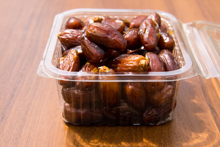 Dried date fruits in plastic container on wooden table