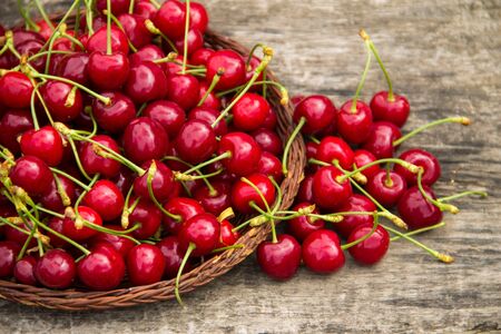 Basket with red sweet cherry fruits on vintage wooden table. Summer fruit season concept
