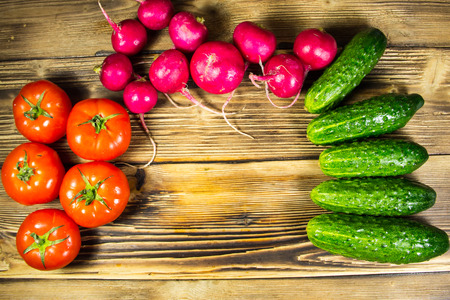 Fresh cucumbers, radishes and tomatoes on the wooden tableの写真素材