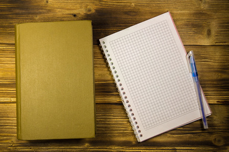 Old closed book, notepad and pen on wooden deskの写真素材