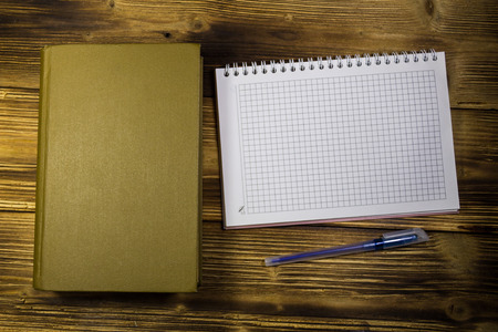 Old closed book, notepad and pen on wooden deskの写真素材