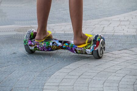 Legs of girl riding on self-balancing mini hoverboard in the city street. Electronic scooter outdoors - personal portable eco transport, gyro scooter, hyroscooter, smart balance wheel, mini segwayの写真素材