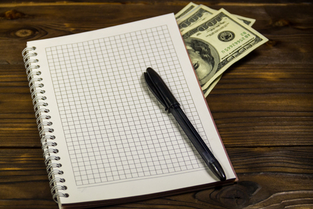 Notebook with ballpoint pen and dollar banknotes on the wooden desk. Saving money conceptの写真素材