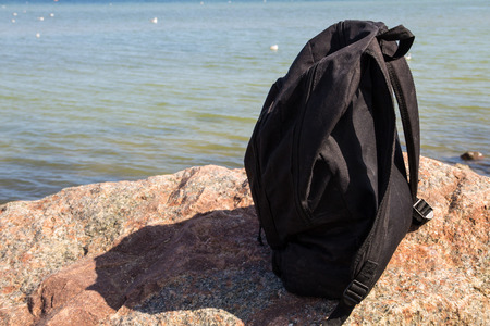 Tourist or traveler backpack on rock with sea shore background. Summer vacations concept