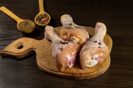 Raw chicken legs with spices on wooden cutting board on a tableの写真素材