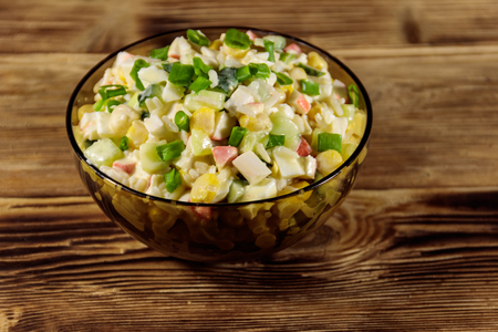 Salad with crab sticks, sweet corn, cucumber, eggs, rice and mayonnaise on wooden tableの写真素材