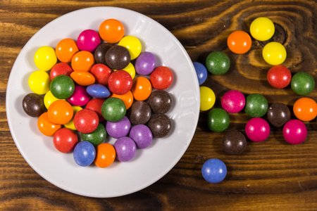 Saucer with colorful button shaped candies filled with chocolate on wooden table. Top viewの写真素材