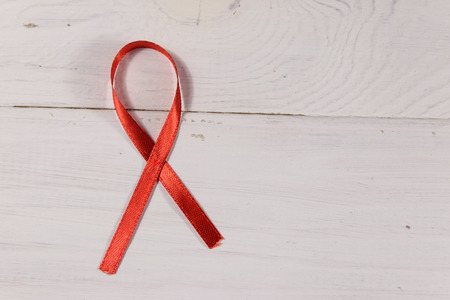 Red AIDS ribbon on white wooden background. Copy space