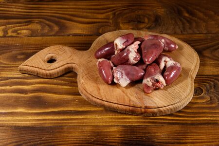 Raw chicken hearts on cutting board on wooden tableの写真素材
