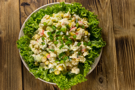 Salad with crab sticks, sweet corn, cucumber, eggs, rice and mayonnaise on wooden table. Top viewの写真素材