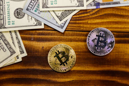 Golden and silver bitcoins and hundred dollar bills on wooden deskの写真素材