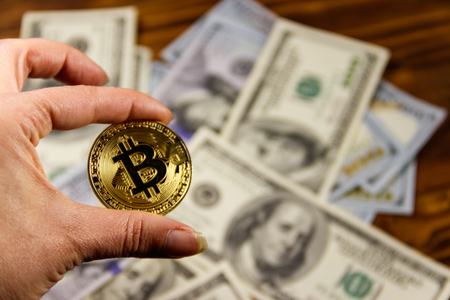 Golden bitcoin in hand against one hundred dollar billsの写真素材
