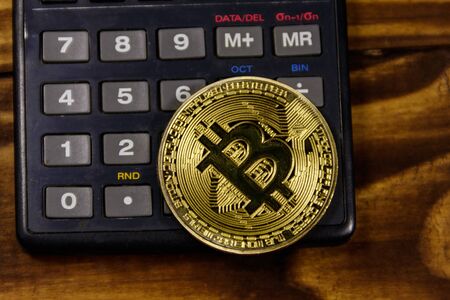 Golden bitcoin and calculator on wooden deskの写真素材
