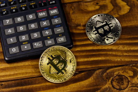 Two bitcoins and calculator on wooden deskの写真素材
