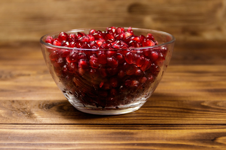 Pomegranate seeds in glass bowl on wooden tableの写真素材