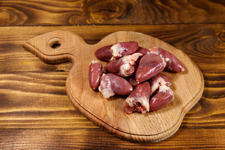 Raw chicken hearts on cutting board on wooden tableの写真素材