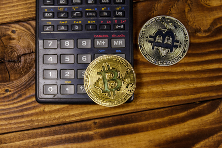 Two bitcoins and calculator on wooden deskの写真素材