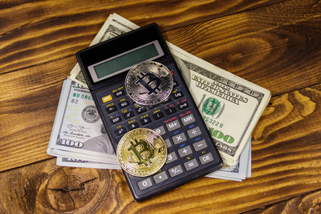 Two bitcoins, calculator and one hundred dollar bills on wooden deskの写真素材