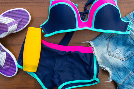 Set of beachwear on wooden background. Sunscreen, swimsuit, jean  shorts and flip-flops. Summer holiday conceptの写真素材