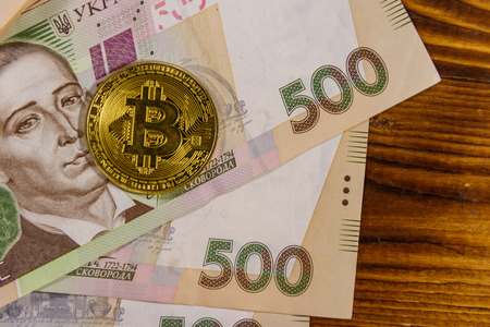 Golden bitcoin and five hundred ukrainian hryvnia bills on wooden backgroundの写真素材